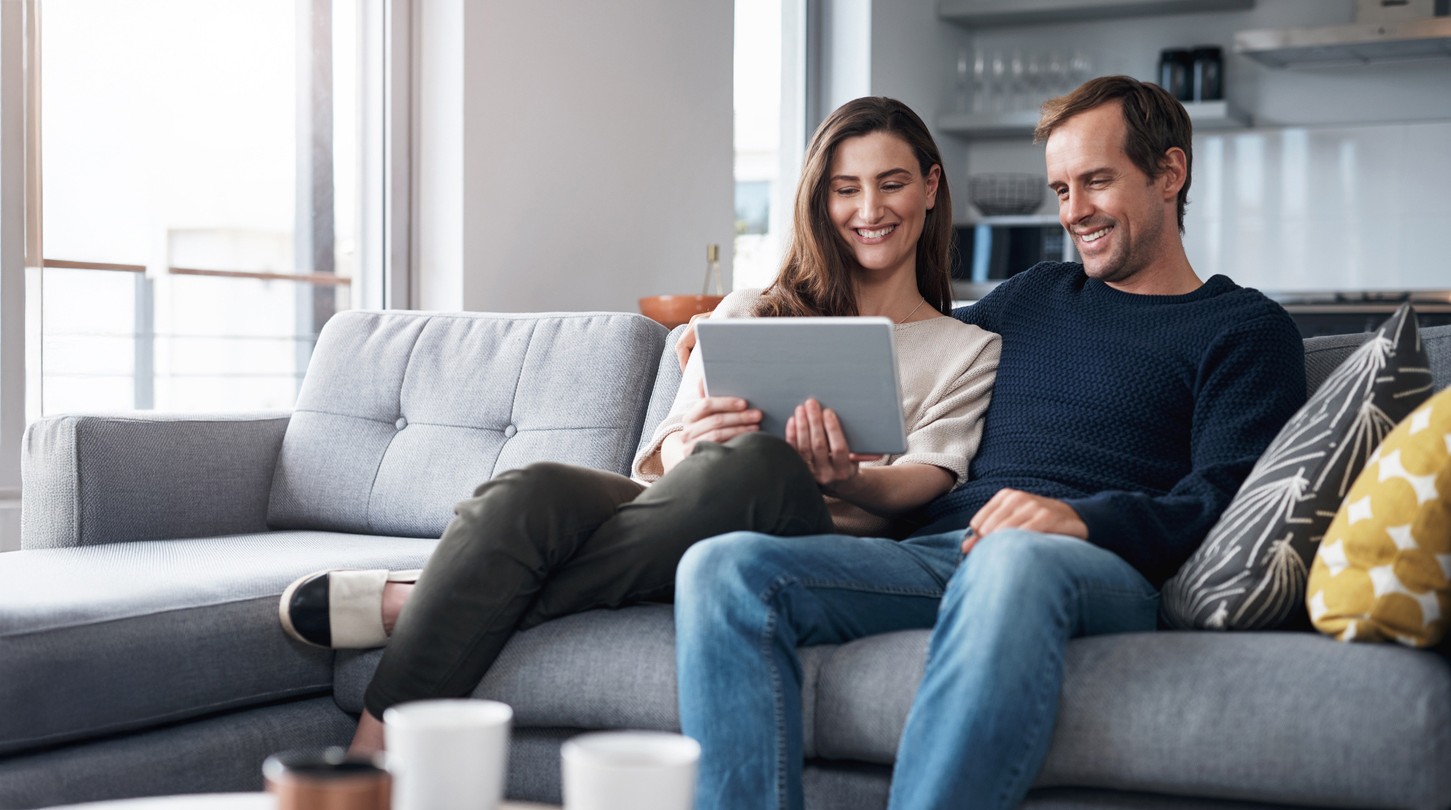 couple laughing looking into tab sitting on sofa